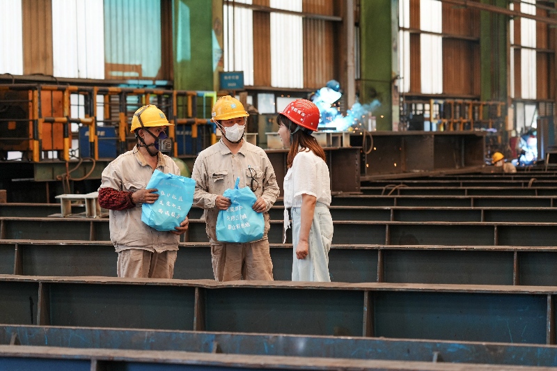 在中建钢构四川有限公司加工车间内，工作人员在为企业工人发放“防暑礼包”