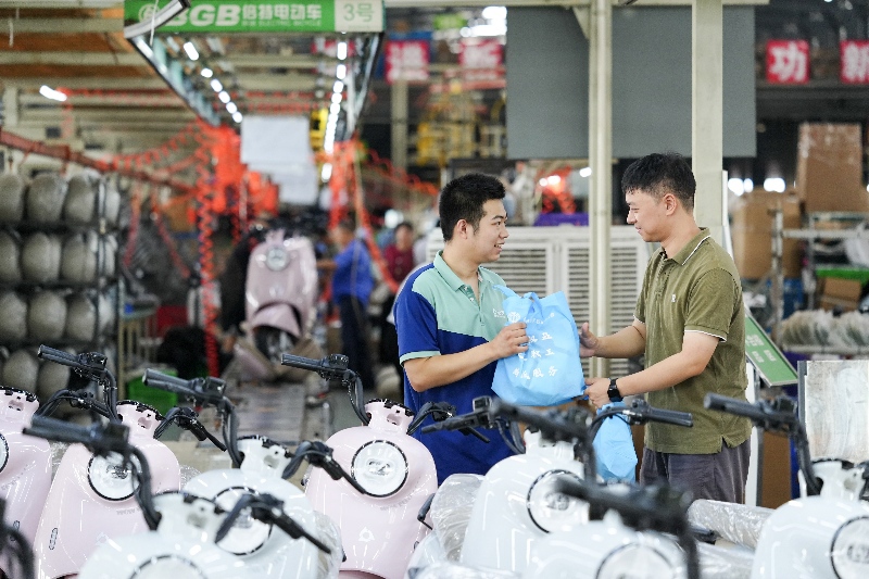 在倍特电动车有限公司生产车间内，工作人员为企业工人发放“防暑礼包”