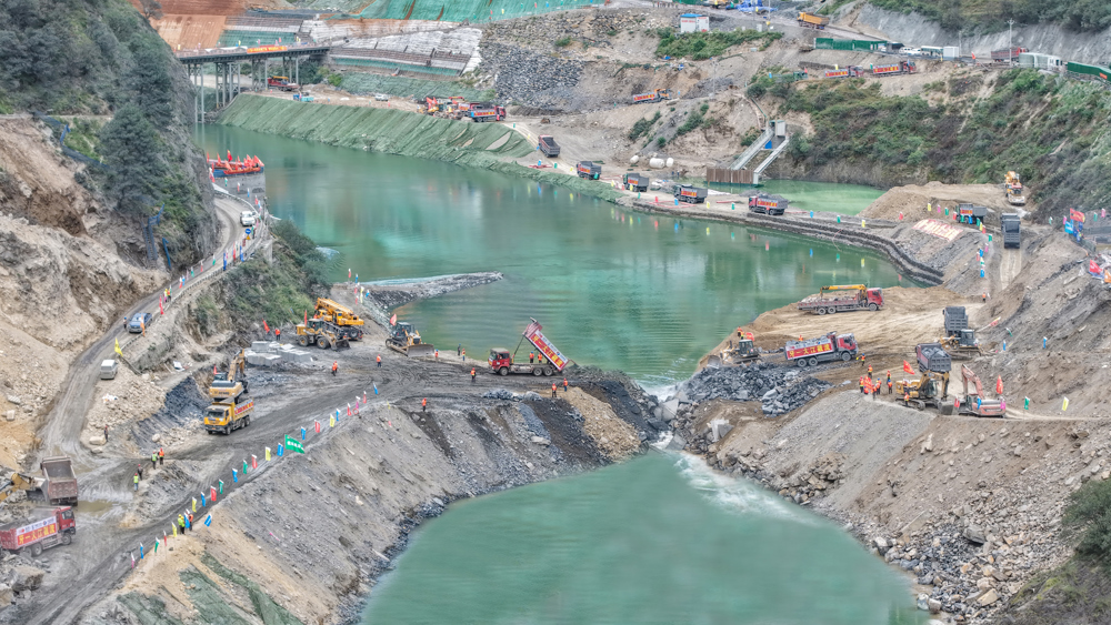 牙根一级水电站龙口合龙即将成功，数十辆自卸汽车来回不间断运输石料进行填筑