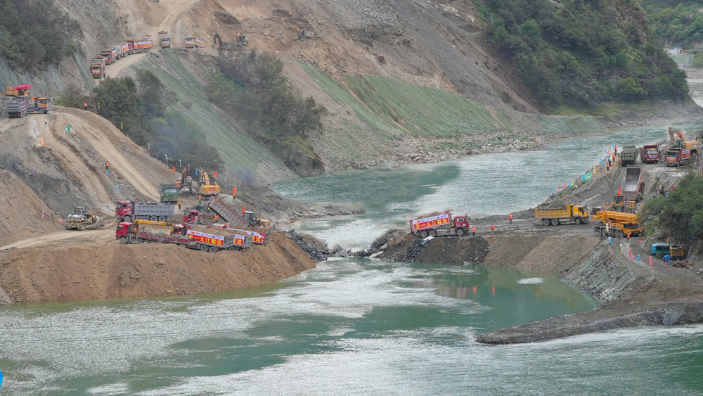 数十辆自卸汽车协同作业将成吨石料抛投进牙根一级水电站主龙口位置